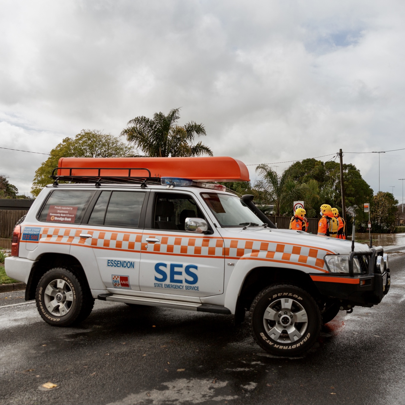 An SES four-wheel drive sits stationary on a flooded road, as three volunteers have a briefing in the background