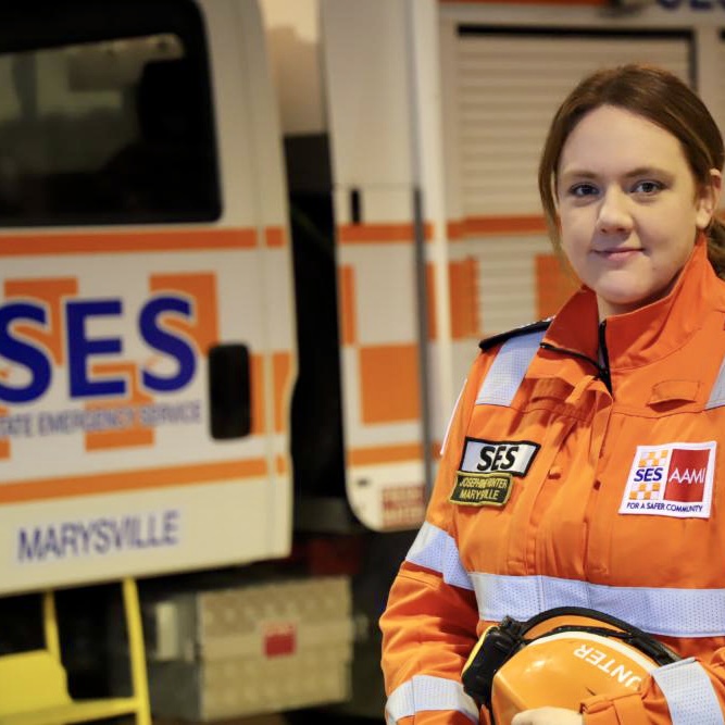 Female volunteer Jo Hunter faces camera in orange SES uniform with an SES truck in the background
