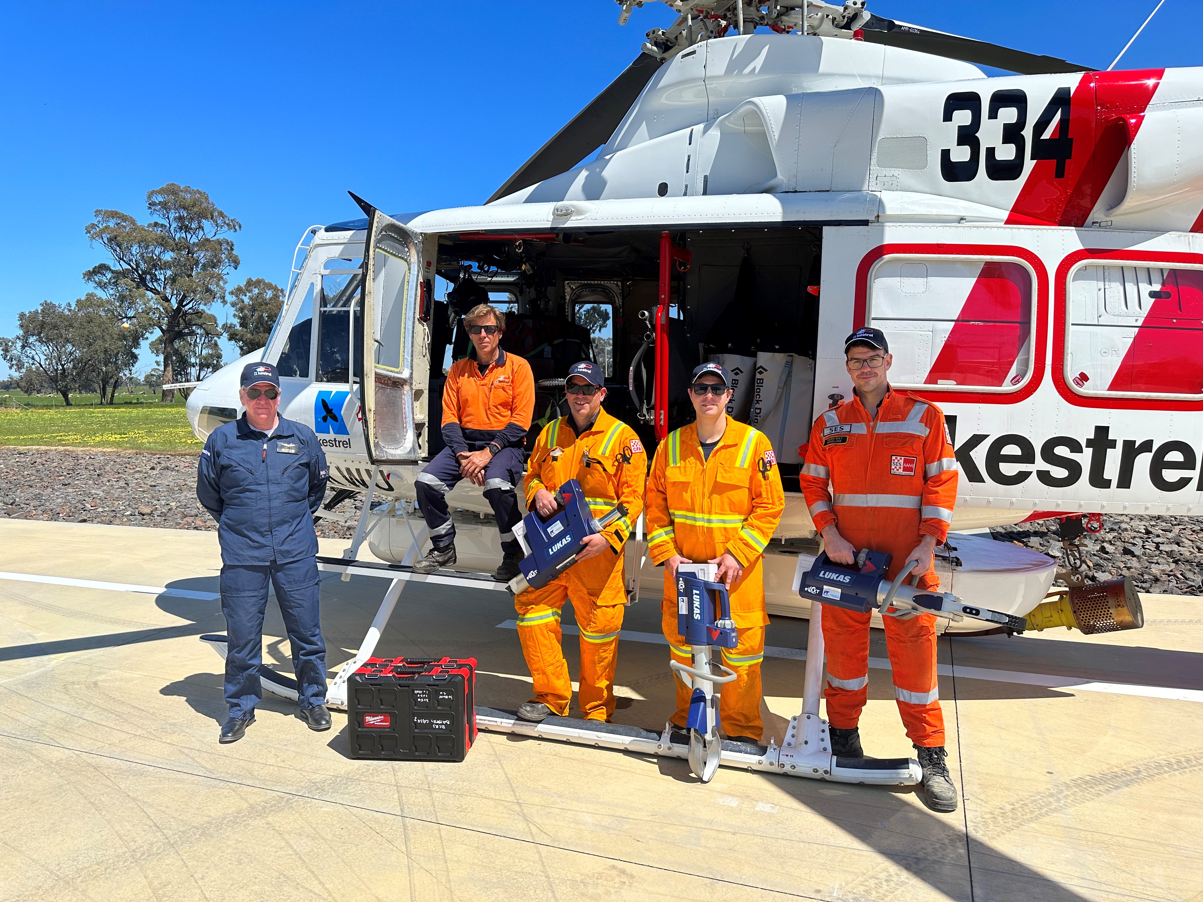 Two CFA members in yellow, a VICSES volunteer in orange, and two members of Shepparton Search and Rescue stand in front of a helicopter